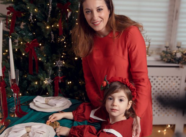 Mamă și fiică la sedinta foto de Craciun la studio în haine roșii stând lângă o masă festivă de Crăciun și un brad împodobit