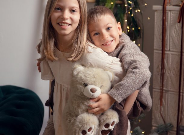Fată și băiat îmbrățișați ținând un urs de pluș la ședința foto de Crăciun la Kinder Studio